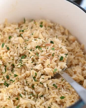 Serving spoon in cast iron pot with rice pilaf and fresh parsley.