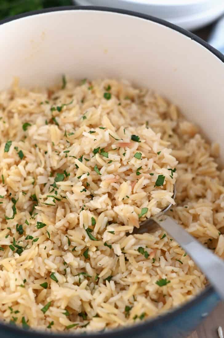 Serving spoon in cast iron pot with rice pilaf and fresh parsley.