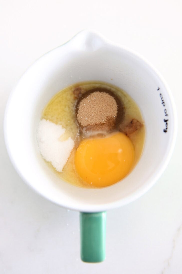 Top down view of egg, butter, brown sugar, granulated sugar in mug.