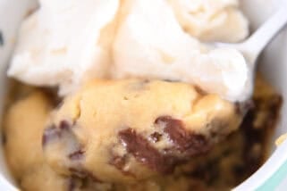 Spoon scooping bite of warm mug cookie with ice cream.