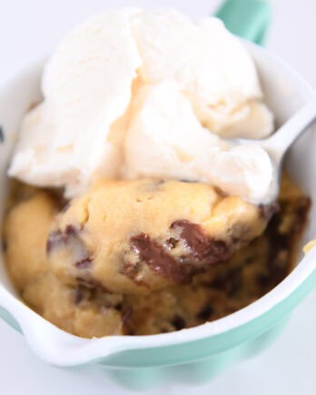 Spoon scooping bite of warm mug cookie with ice cream.