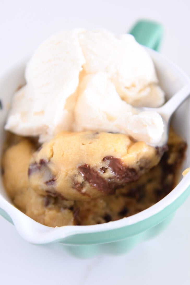 Spoon scooping bite of warm mug cookie with ice cream.