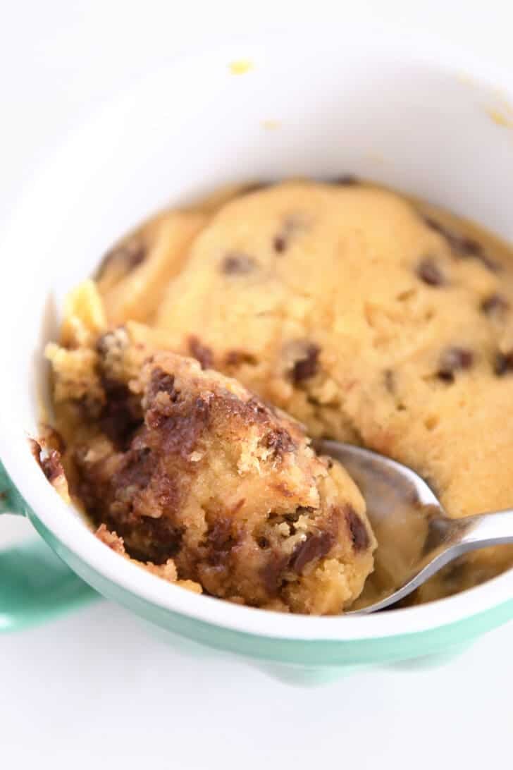 Spoon scooping bite of warm chocolate chip cookie in mug.