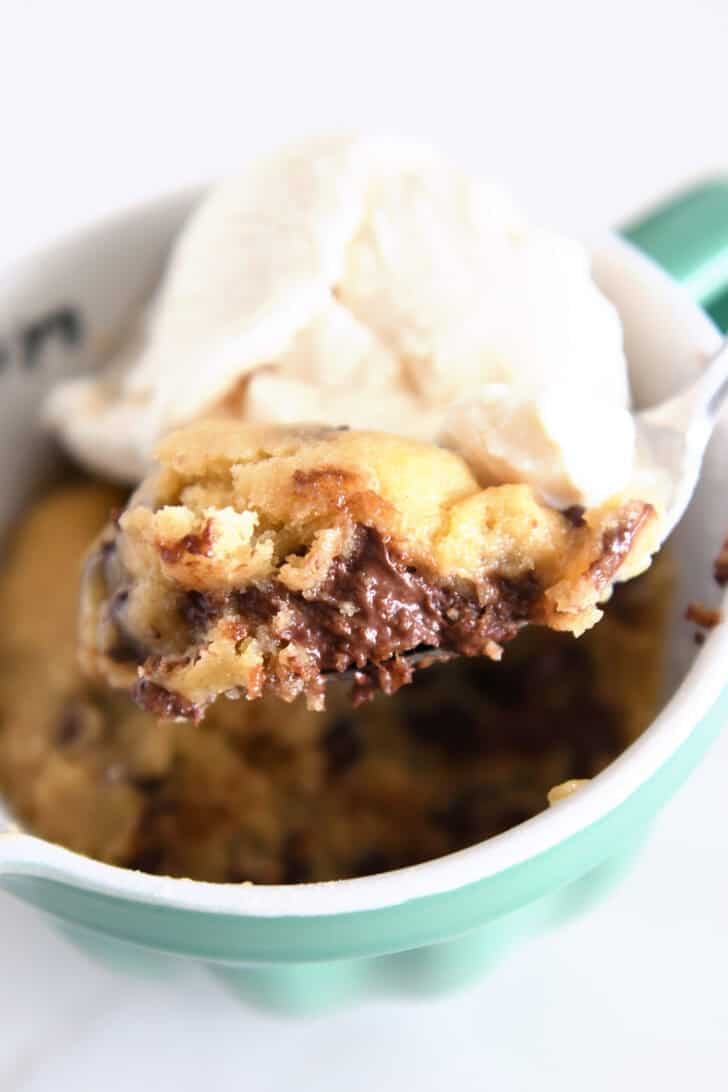 Spoon scooping bite of chocolate chip cookie and ice cream in mug.