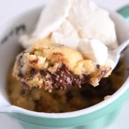 Spoon scooping up bite of warm chocolate cookie in mug with ice cream.