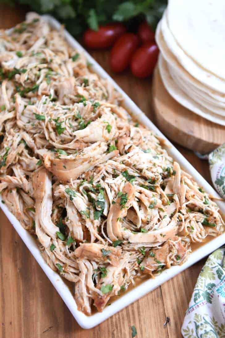 Top down view of a white platter with shredded chicken in sauce topped with chopped cilantro.