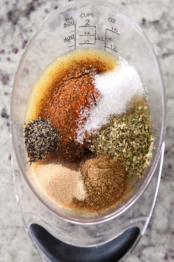 Top down view of a plastic measuring cup full of various spices.