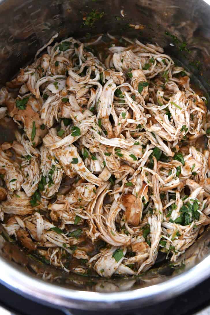 Top down view of a metal bowl with shredded chicken in a sauce and topped with chopped cilantro.