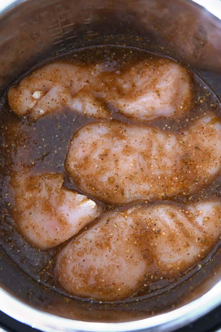 Top down view of raw chicken breasts in red sauce in a metal bowl.