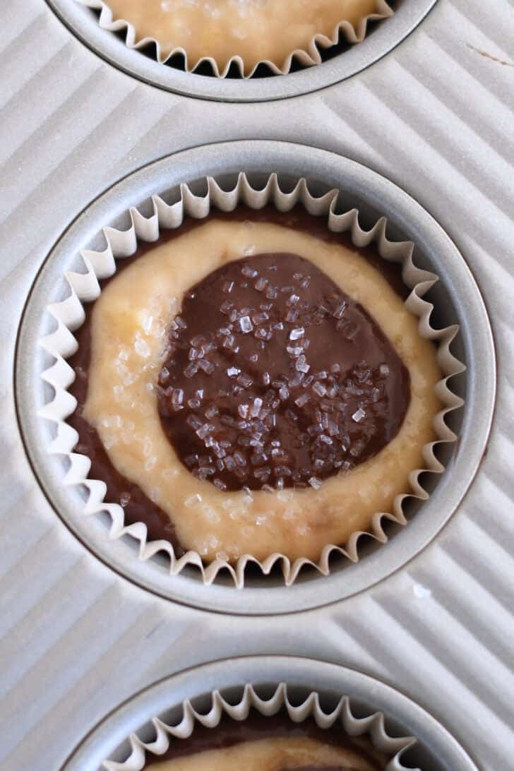 Coarse sugar sprinkled on top of banana muffin batter in lined muffin tin.