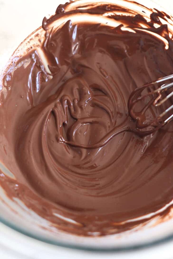 Glass bowl with creamy chocolate mixture and whisk.