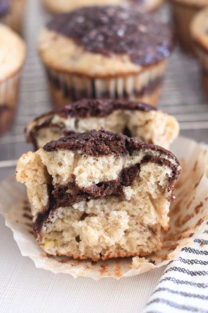Banana muffin split in half with chocolate ribbon swirl running halfway through the baked muffin.