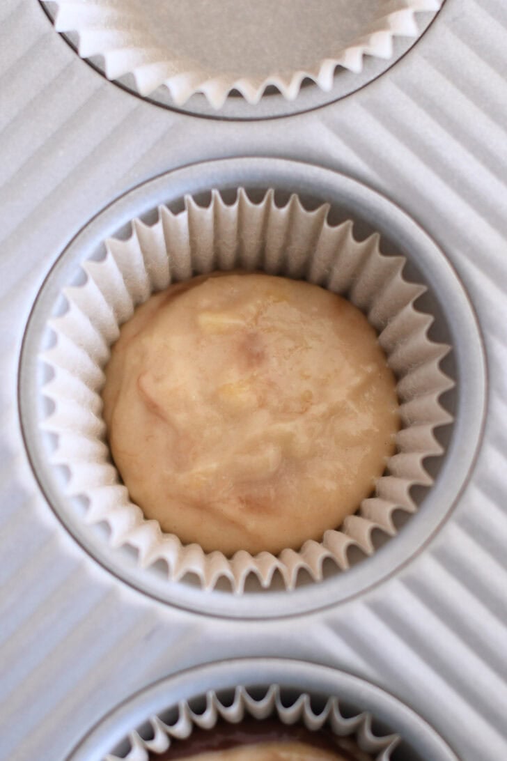 Muffin tin liner with scoop of banana muffin batter.
