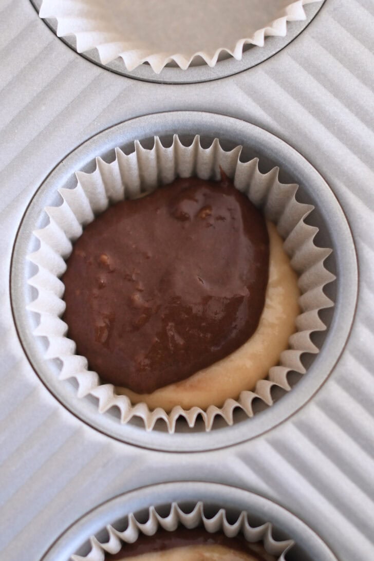 Muffin tin liner with scoop of banana muffin batter and chocolate banana muffin batter.