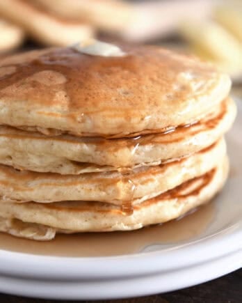 Stack of four pancakes on white plates with syrup drizzled down the side.