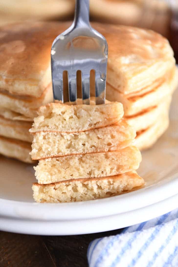 Two stacked white plates with four old-fashioned pancakes with triangular stacked bite to the side.