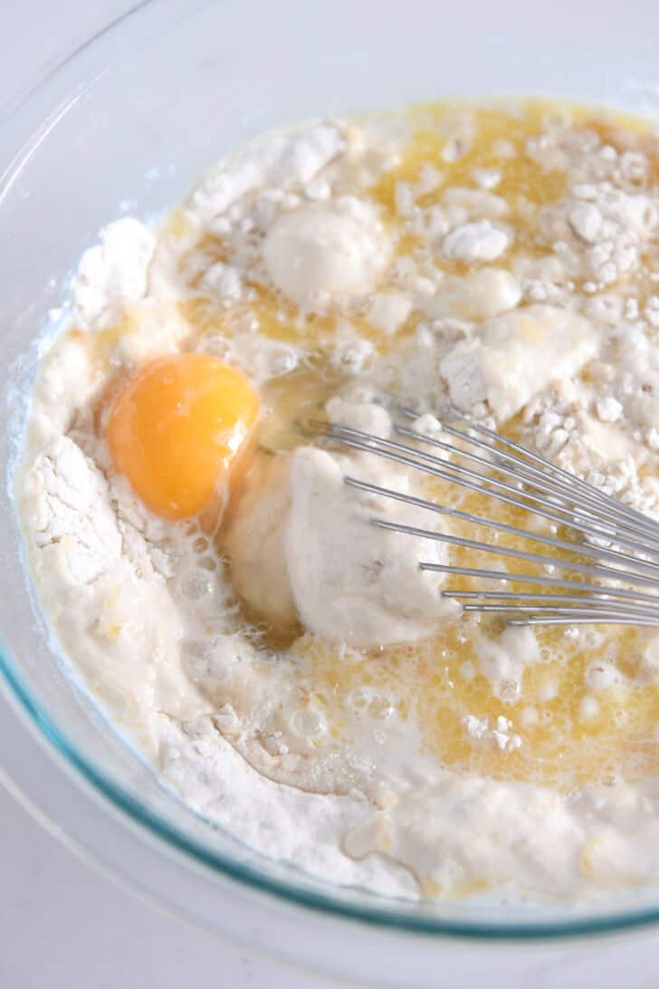 Glass bowl with whisk mixing egg, milk, and dry ingredients for pancakes.