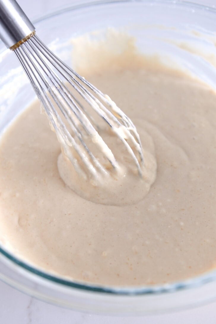 Whisk in glass bowl with light-colored pancake batter.