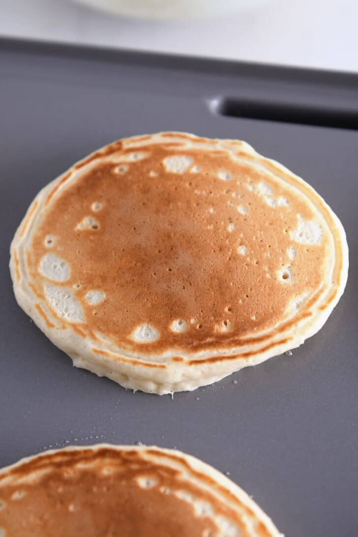 Pancaked flipped and golden cooking on gray nonstick griddle.