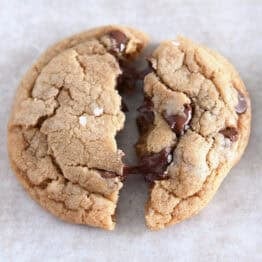 Soft melty brown butter chocolate chip cookie split in half on parchment paper.