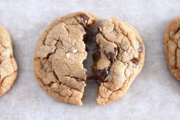 Soft melty brown butter chocolate chip cookie split in half on parchment paper.