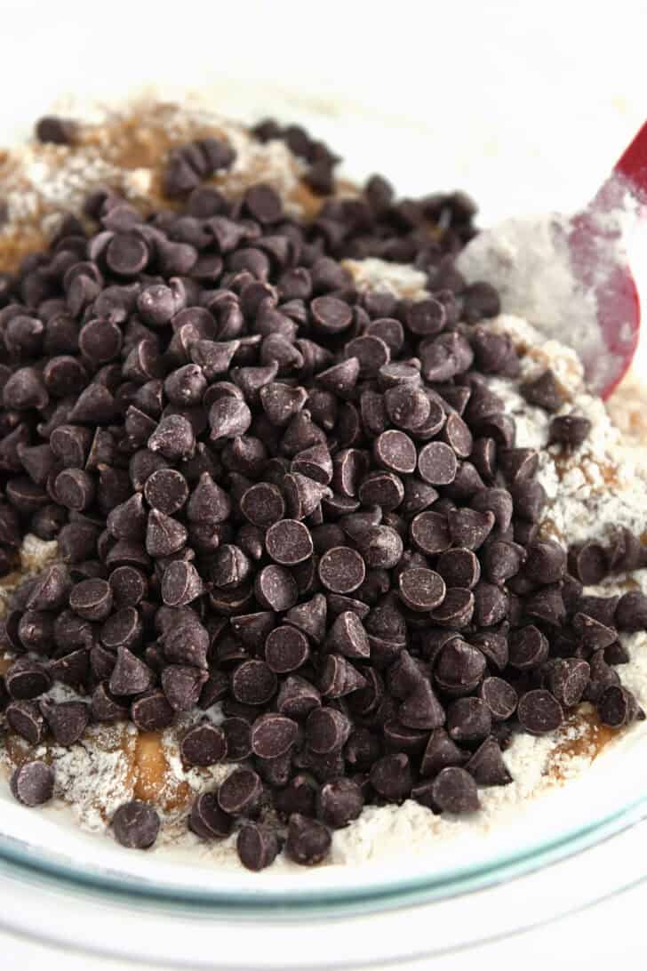 Semisweet chocolate chips in glass bowl with dry ingredients and red silicone spatula.