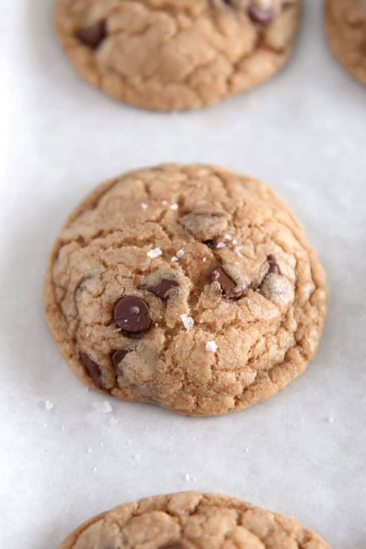 Sea salt flakes on top of baked brown butter chocolate chip cookies on parchment lined baking sheet.