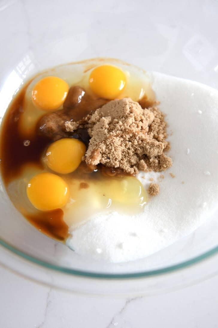 Glass bowl with eggs, brown sugar, white sugar and oil.