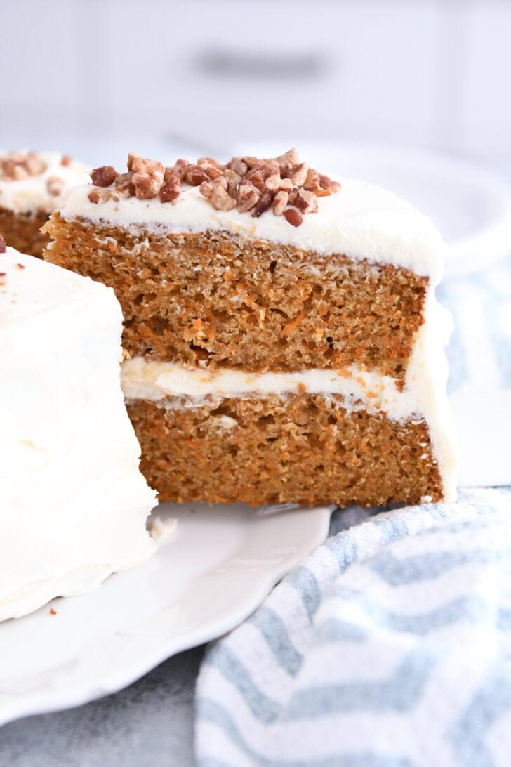 Slice of carrot cake being pulled out of whole frosted carrot cake.