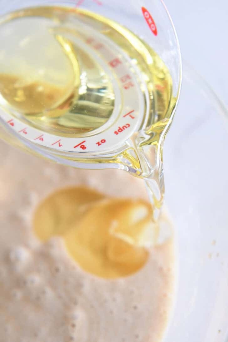Drizzling oil into carrot cake batter in glass bowl.