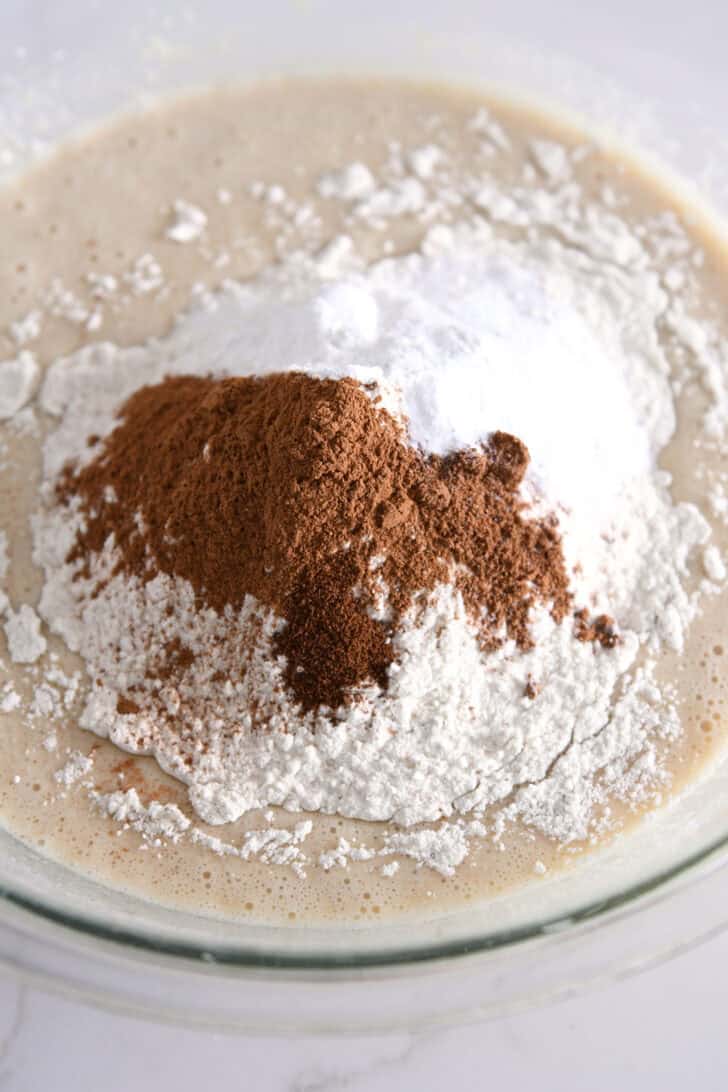 Glass bowl with wet ingredients, flour, cinnamon, nutmeg and cloves.