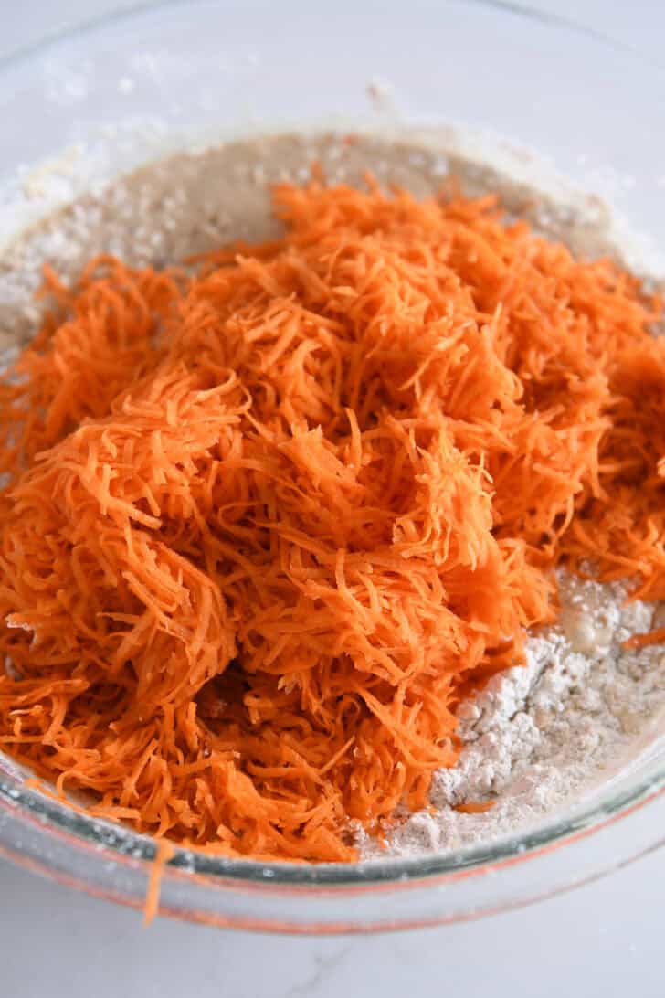 Glass bowl with cake batter and finely shredded carrots.