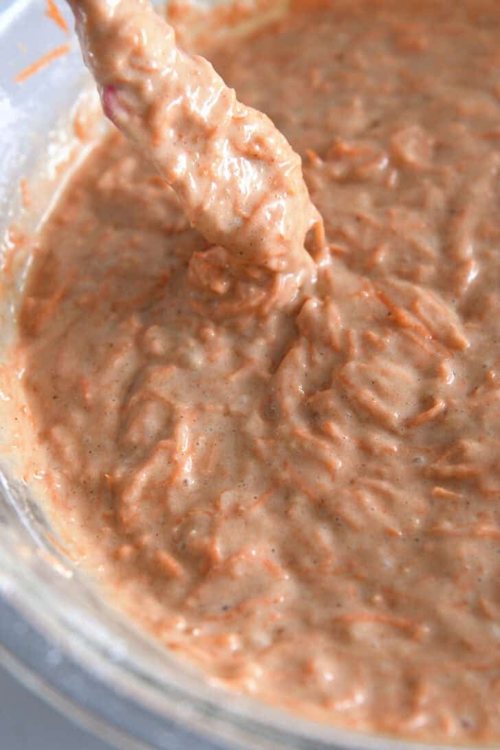 Small spatula drizzling carrot cake batter out of bowl with cake batter.