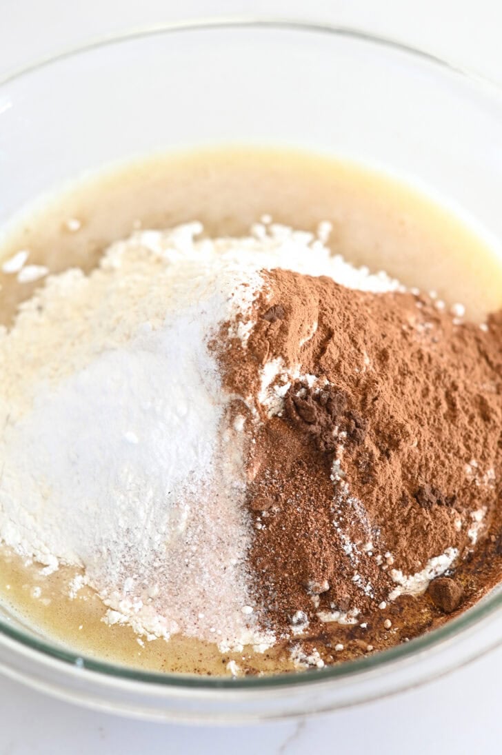 Top down view of a glass bowl with spices, flour, and cake batter.