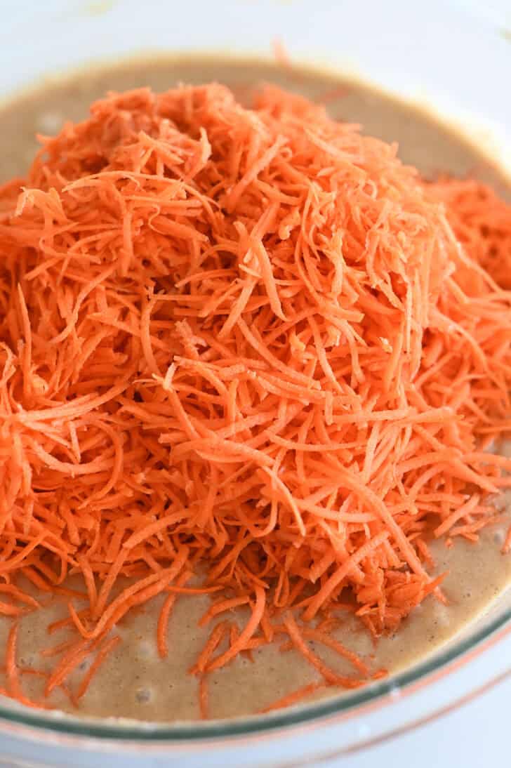 Top down view of a glass bowl with carrot cake batter and shredded carrots.