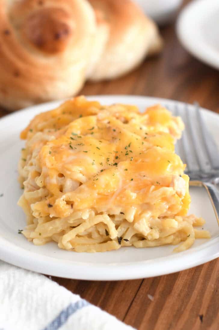 Square of cheese-topped cheesy chicken spaghetti on white plate with fork.