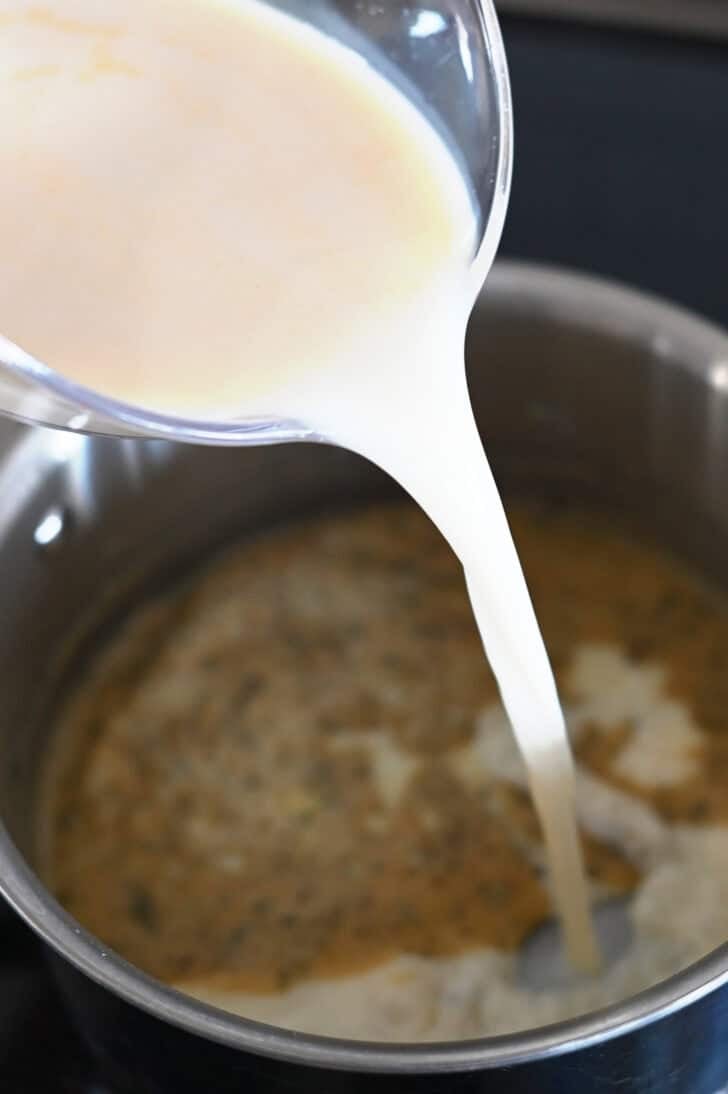 Pouring milk and broth into saucepan with flour and butter roux.