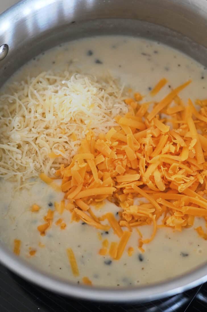 Shredded cheddar and Parmesan cheeses in creamy sauce in saucepan.