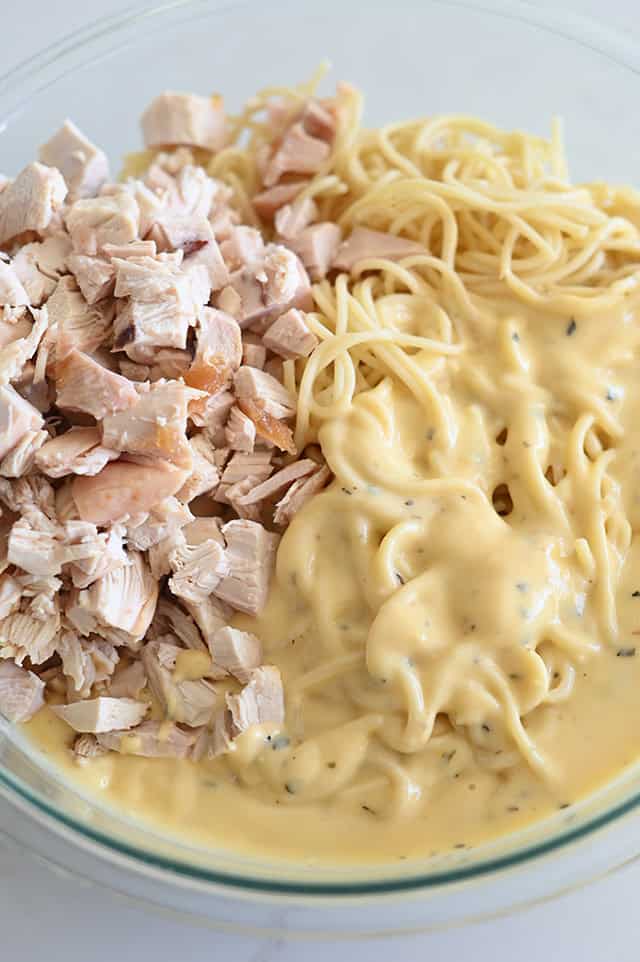Glass bowl with cooked spaghetti noodles, cooked chicken, and homemade cheese sauce.