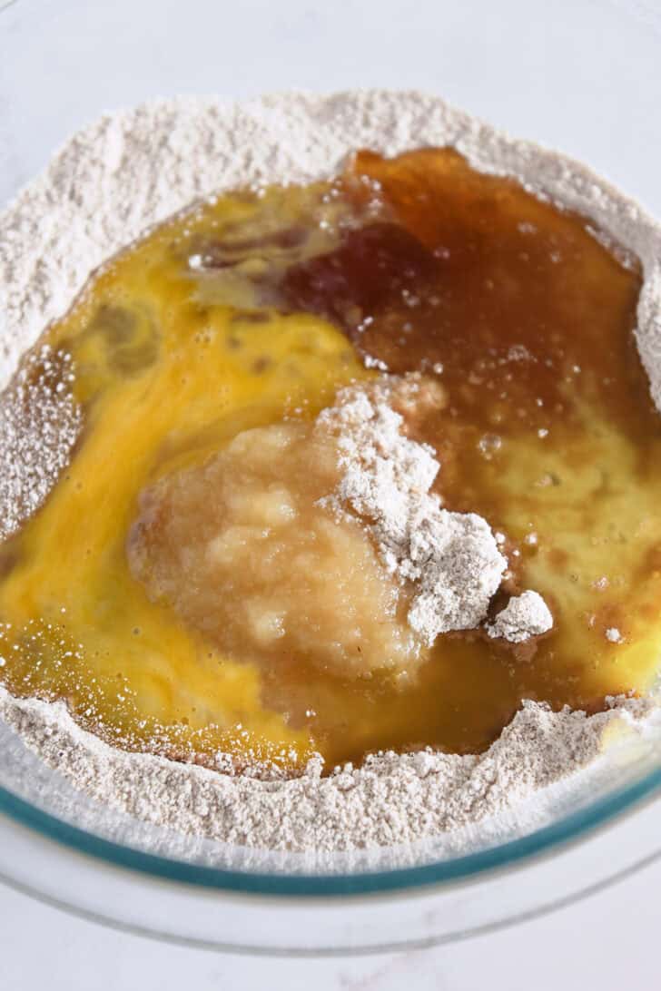 Glass bowl with whole wheat flour, egg, applesauce, butter and vanilla.