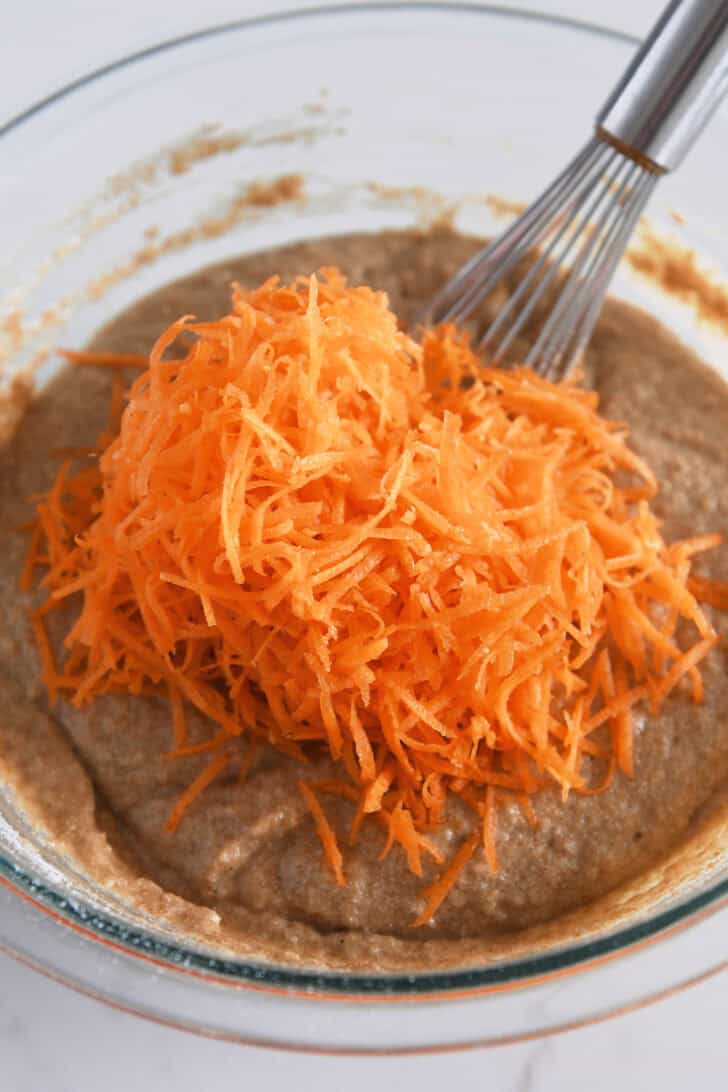 Shredded carrots in bowl with carrot cake muffin batter.