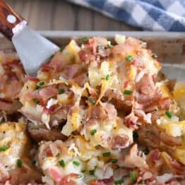 Spatula scooping serving of cheesy smashed potatoes off of half sheet pan.