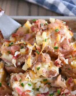Spatula scooping serving of cheesy smashed potatoes off of half sheet pan.