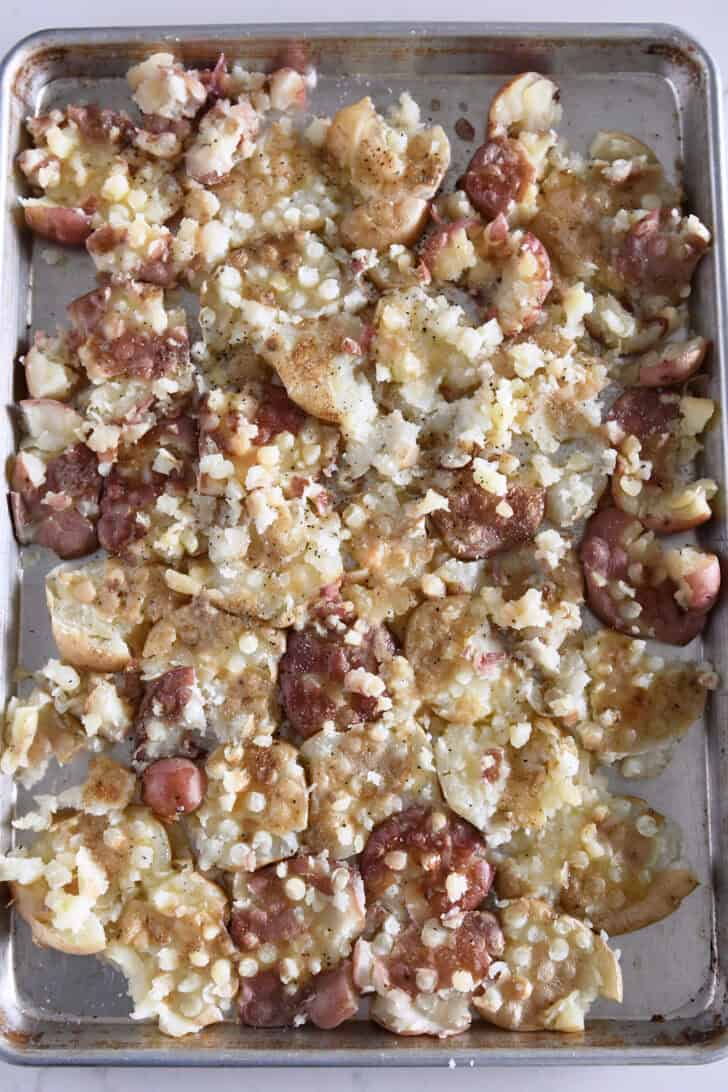 Top down view of smashed potatoes drizzled with butter and salt and pepper on half sheet pan.
