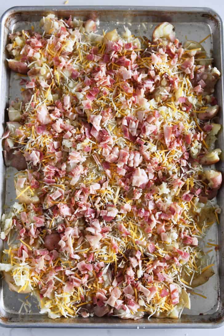Top down view of smashed potatoes topped with cheese and bacon on half sheet pan.