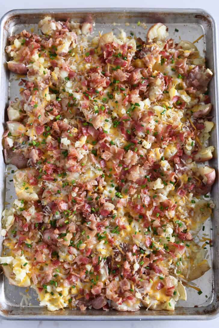 Top down view of cheesy garlic smashed potatoes topped with chives on half sheet pan.
