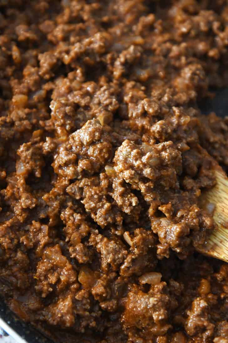 Top down view of cooked taco meat and a wooden spoon scooping some meat out.