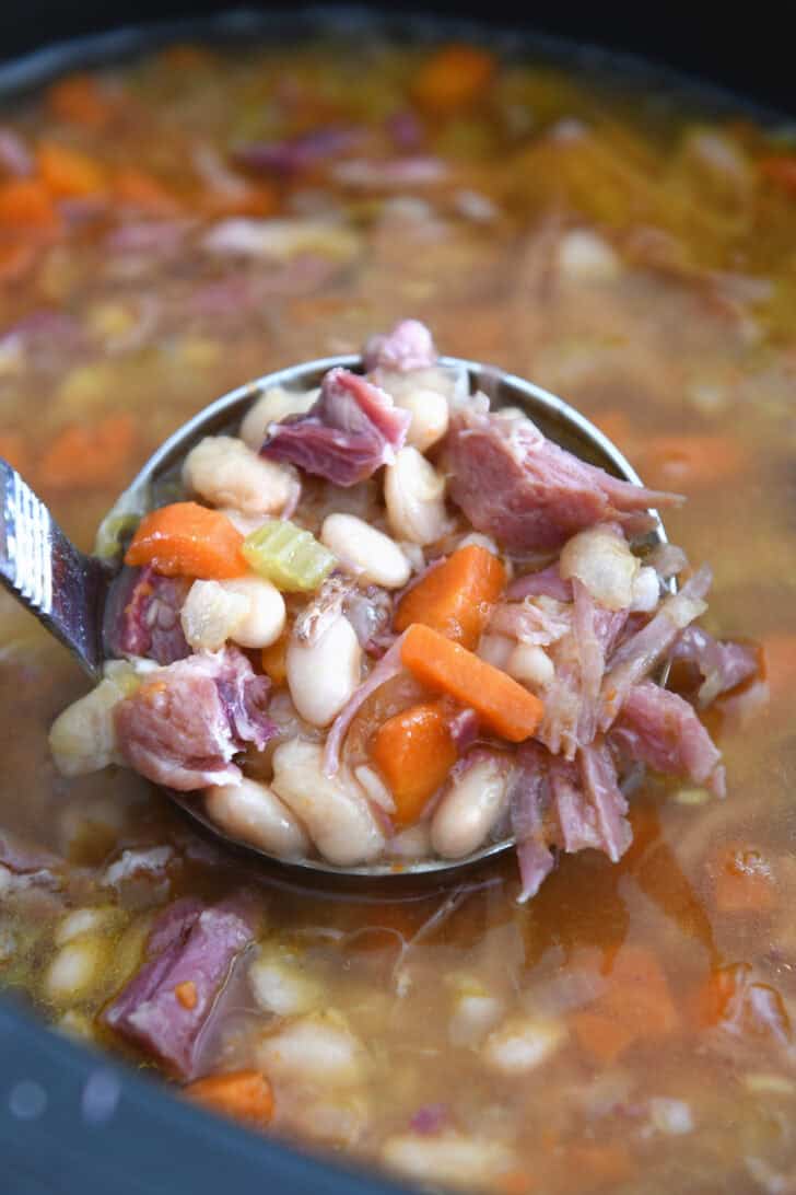Ladle with white beans, carrots, celery, ham and broth.