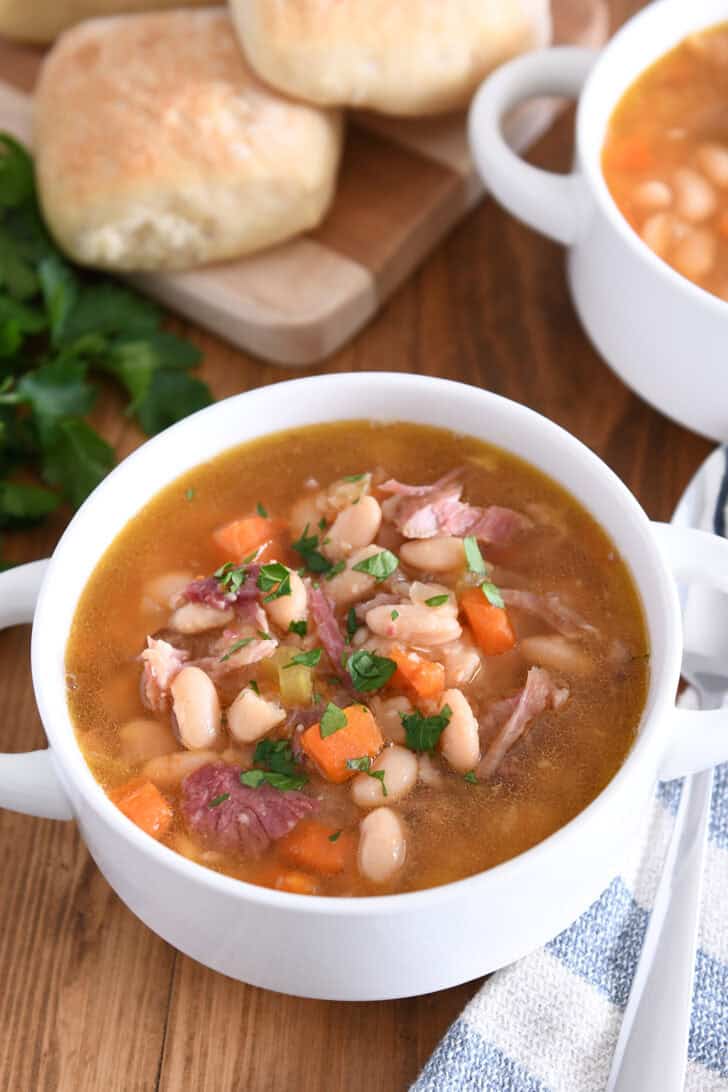White bowl with handles with ham and bean soup.