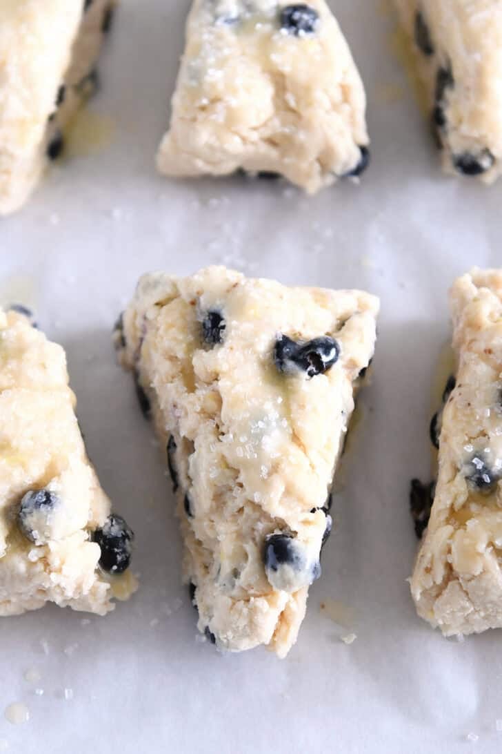 Unbaked lemon blueberry scones brushed with butter and sprinkled with coarse sugar.